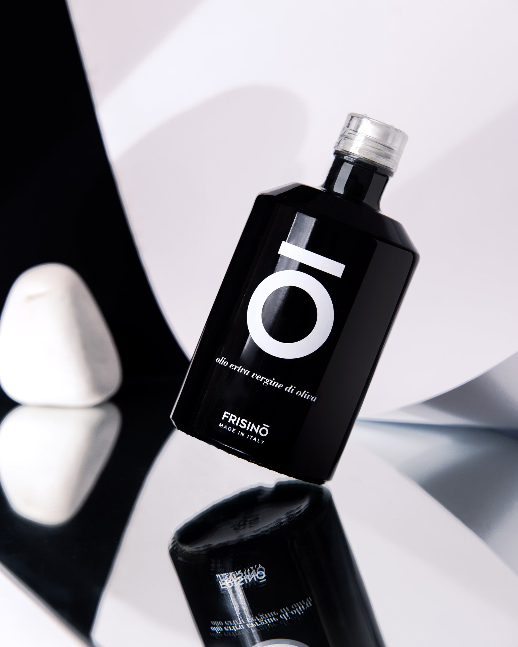 Frisino black bottle of Coratina extra virgin olive oil limited edition on reflective surface with white pebble