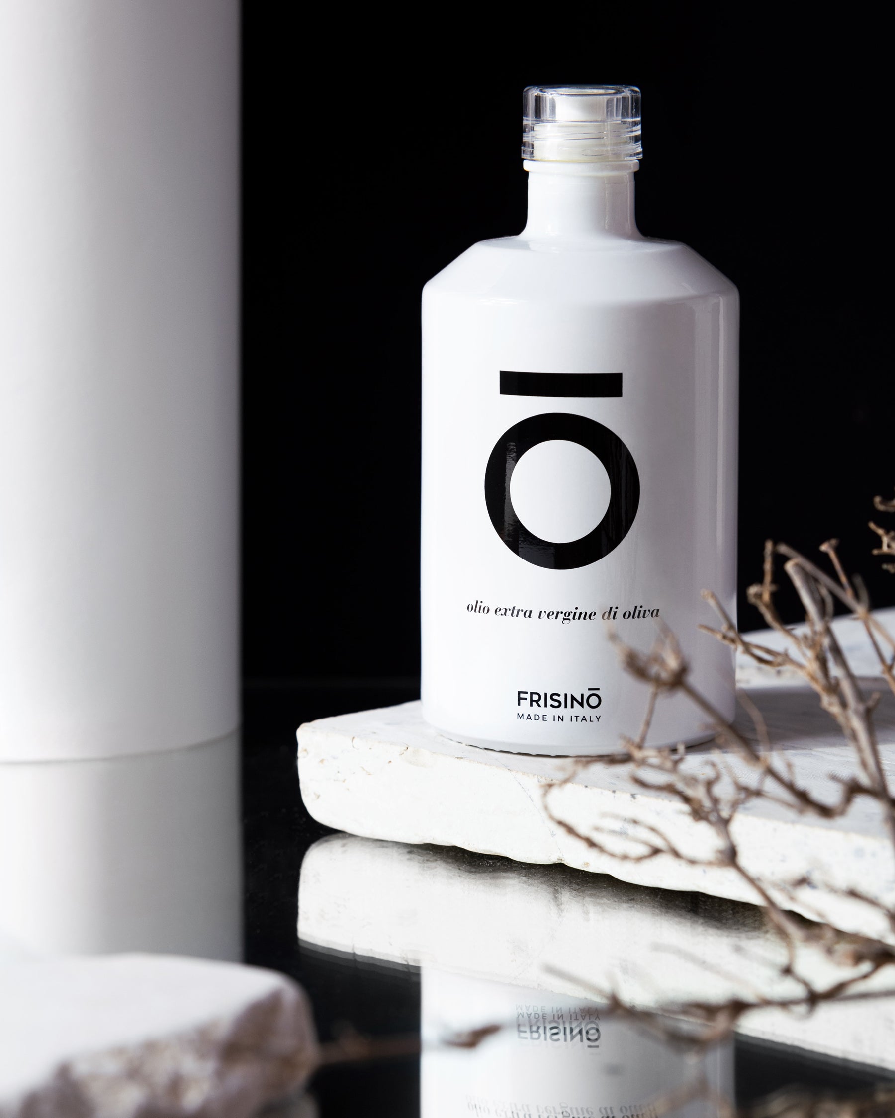 White Frisino Evo Oil Limited extra virgin olive oil bottle on pale stone with dry twigs against a black background