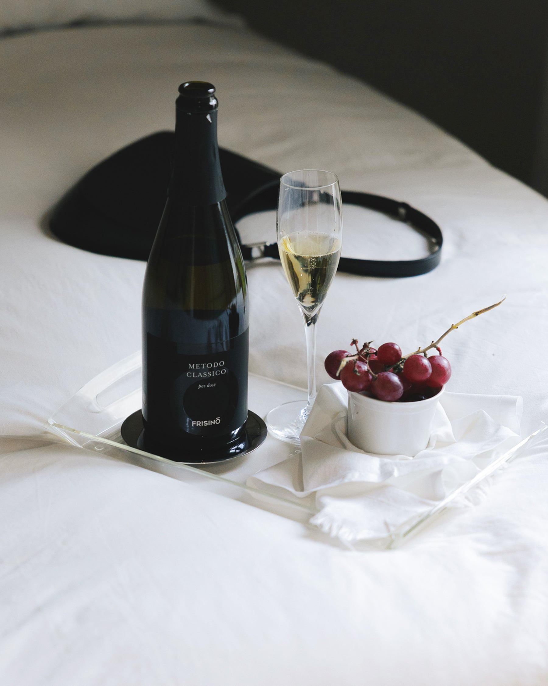 Frisino Metodo Classico Pas Dosé sparkling wine bottle with filled flute and red grapes on a tray over white linen
