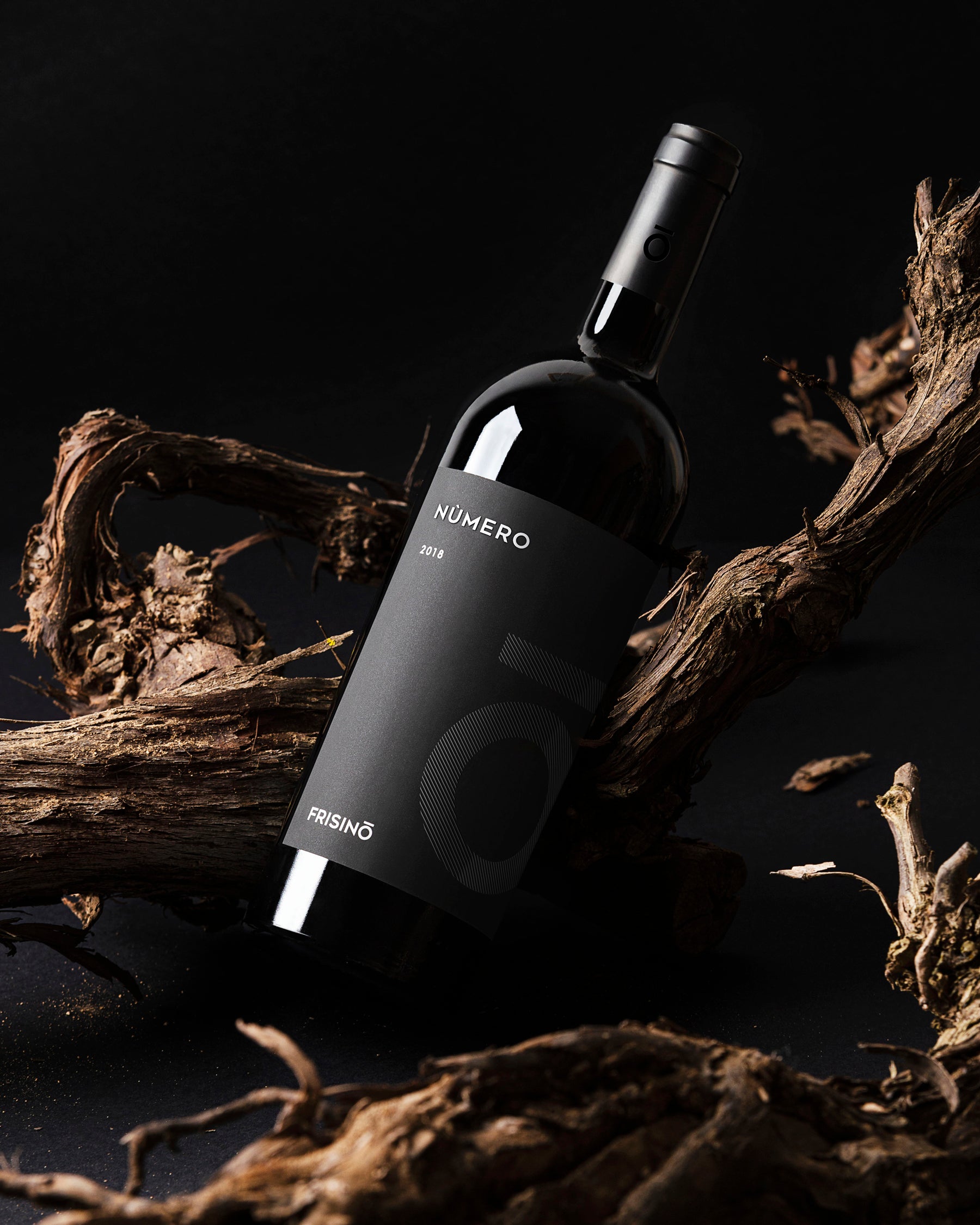 Bottle of Nùmero 2018 Primitivo Puglia IGP by Frisino, black label resting on vine branches against a dark background