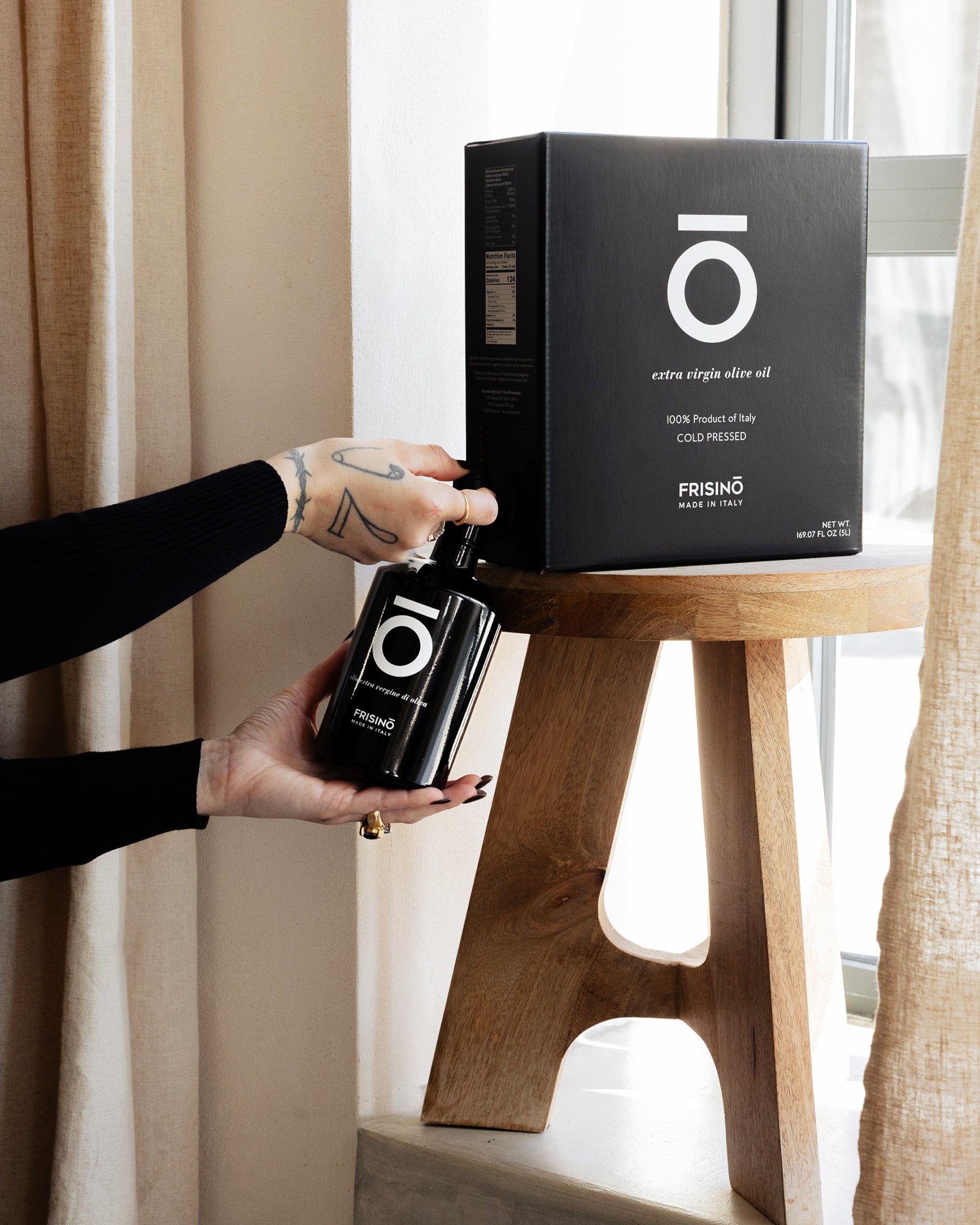 Frisino 5 L bag in box of Coratina extra virgin olive oil with black dispenser bottle filled by hand on a wooden stool