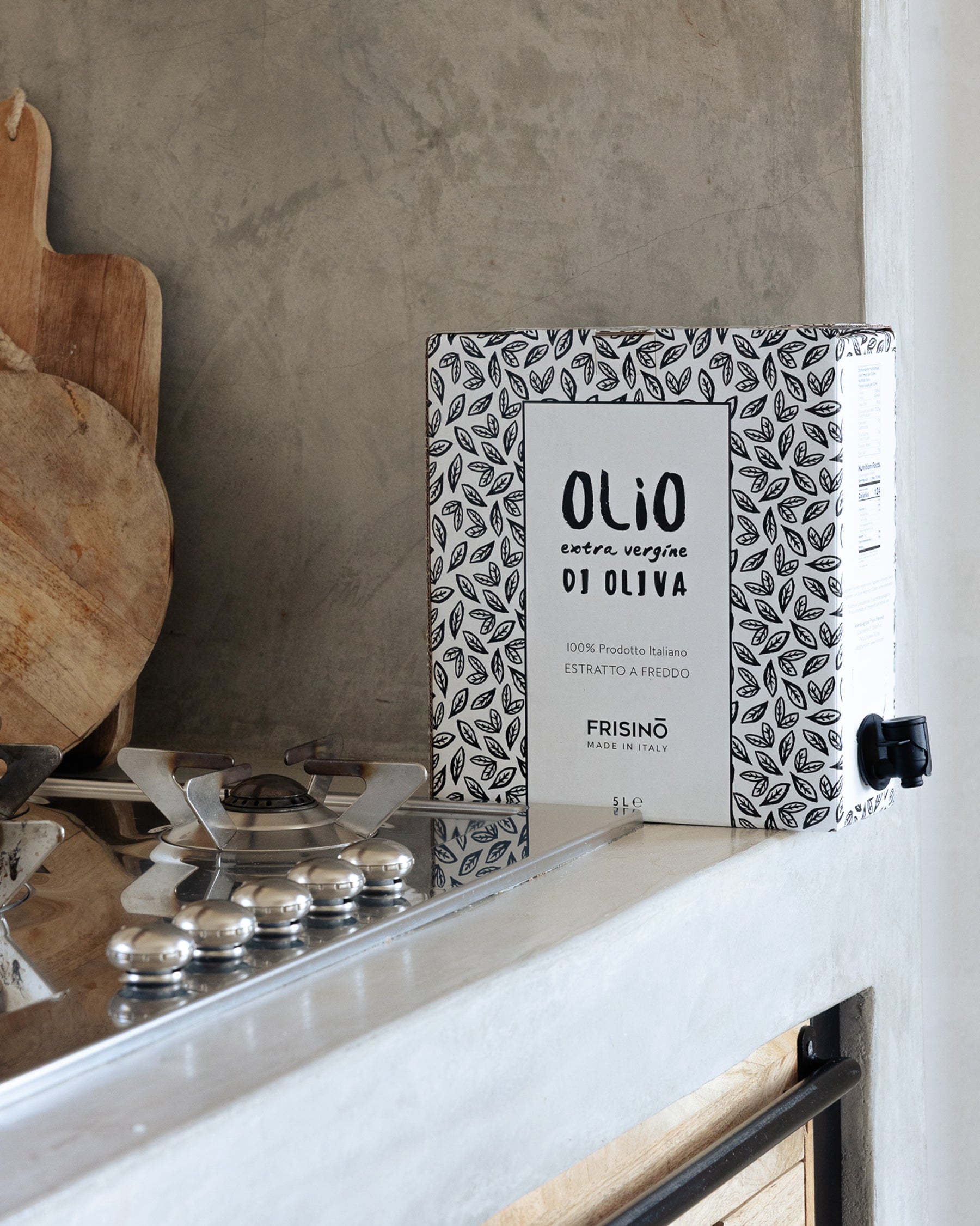 5L Frisino extra virgin olive oil bag-in-box with tap and leaf pattern, on a kitchen counter beside a hob and wooden boards