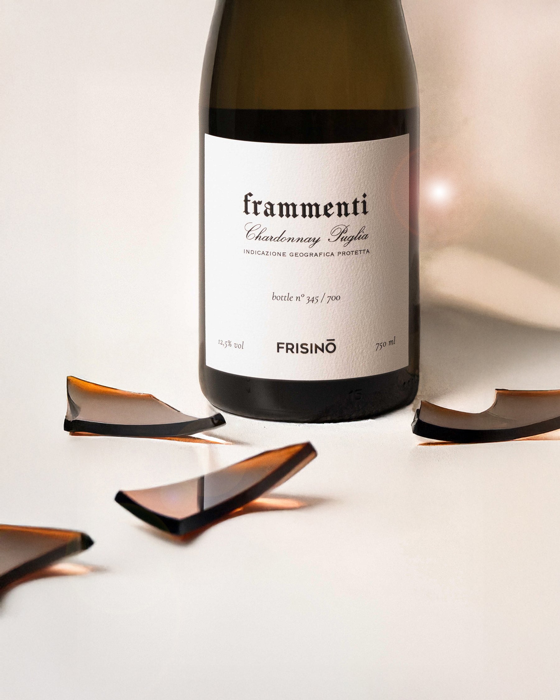 Bottle of Frisino Frammenti Chardonnay Puglia IGP, 750 ml, with amber glass shards on a light background