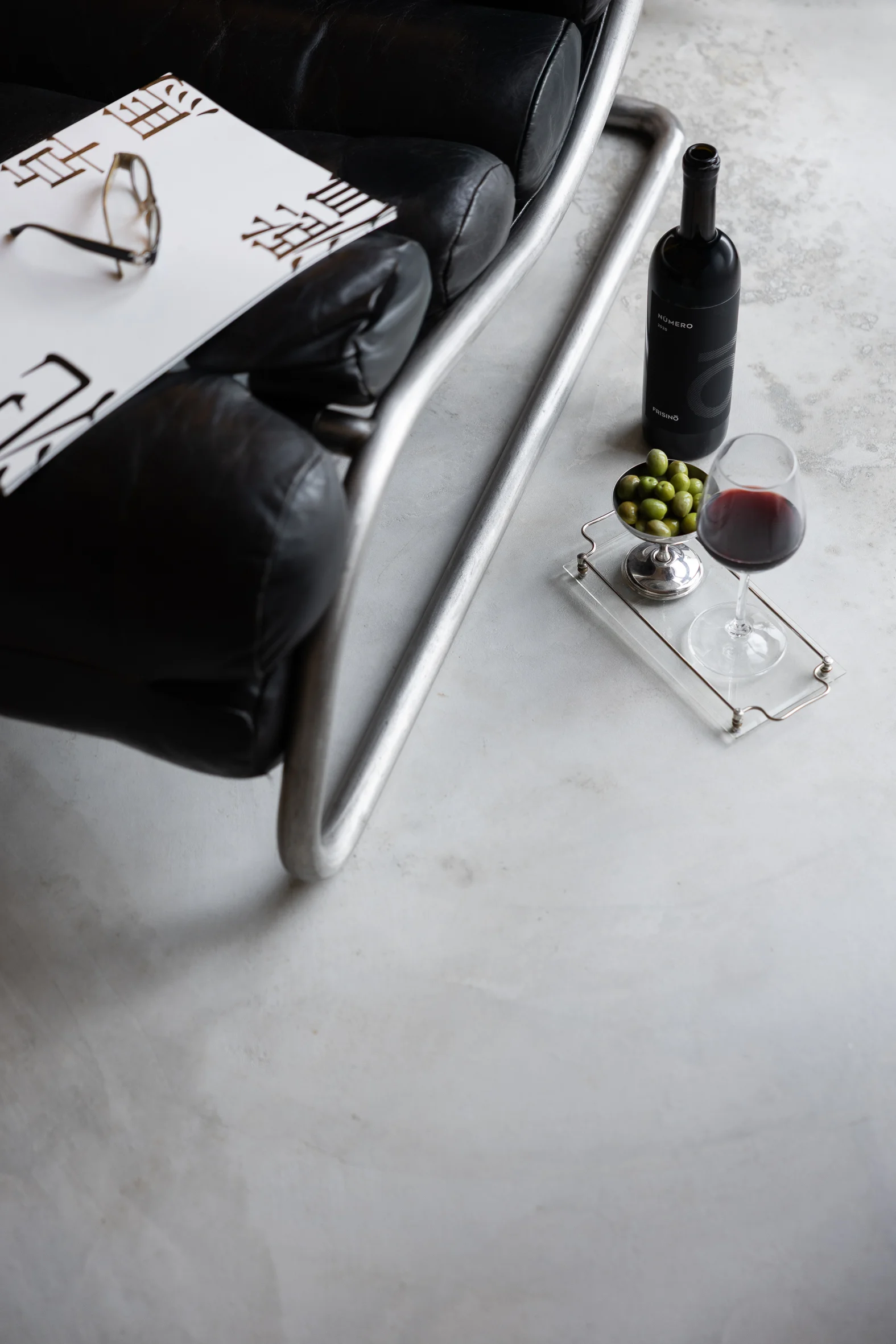Frisino Numero 2020 wine bottle with a glass of red and green olives on a tray, beside a black leather sofa